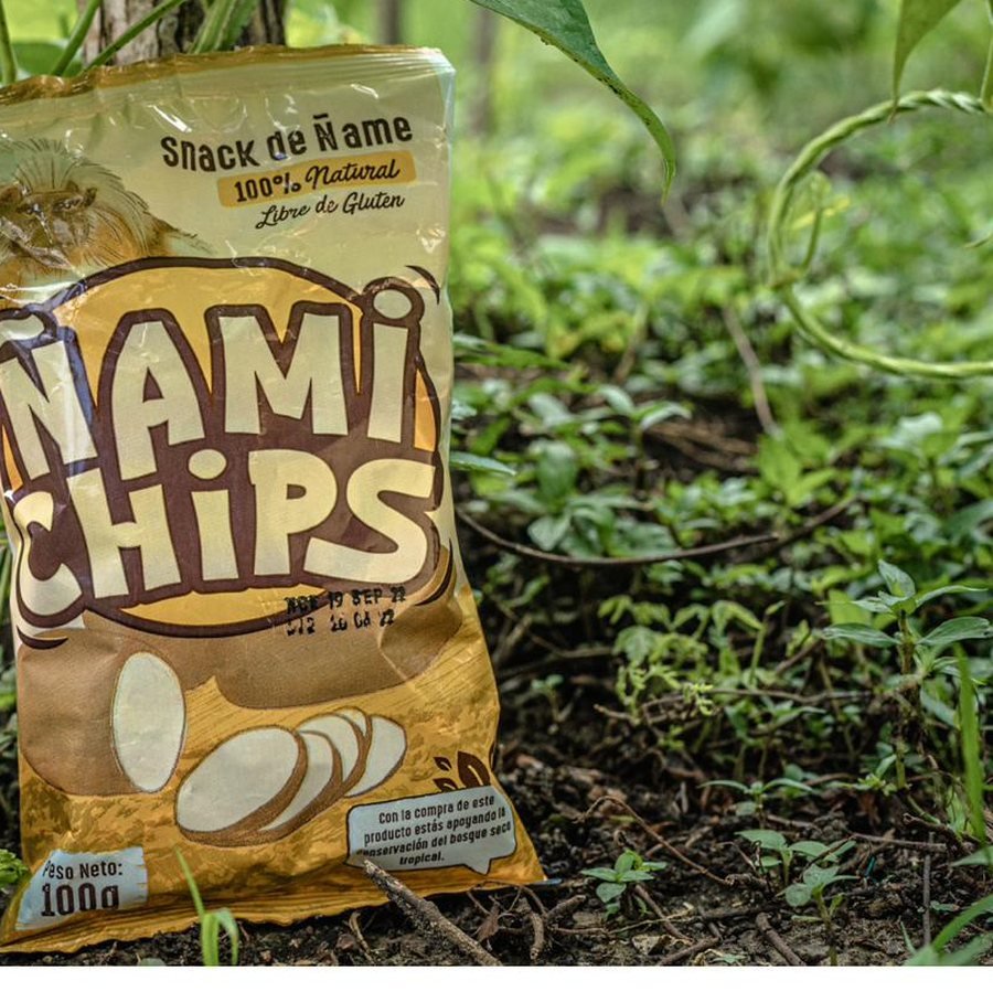 Paquete de ÑamiChips de 100 gramos junto a un ñame en el bosque